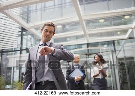 Stock Photo - Businessman looking at watch walking out of office building. Fotosearch