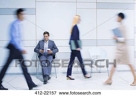 Businessman sitting using cell phone in office building View Large Photo Image Stock Photo - Businessman sitting using cell phone in office building. Fotosearch