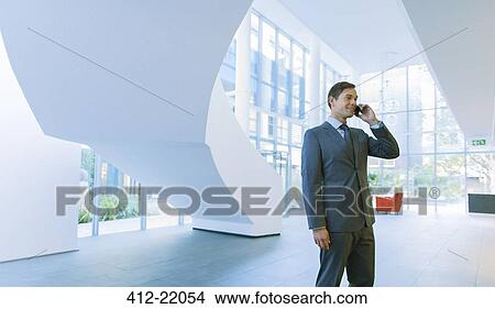 Picture - Businessman talking on cell phone in office building. Fotosearch