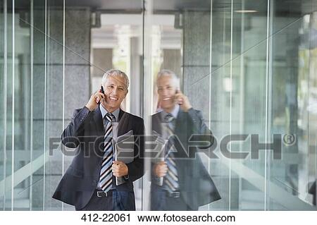 Businessman talking on cell phone in office building View Large Photo Image Stock Image - Businessman talking on cell phone in office building. Fotosearch
