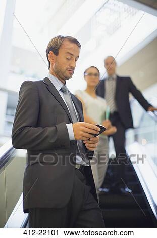 Businessman using cell phone on escalator View Large Photo Image Stock Image - Businessman using cell phone on escalator . Fotosearch