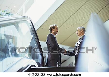 Businessmen shaking hands at top of stairs of office building View Large Photo Image Stock Photo - Businessmen shaking hands at top of stairs of office building. Fotosearch