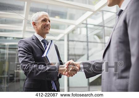 Stock Photo - Businessmen shaking hands in office building. Fotosearch