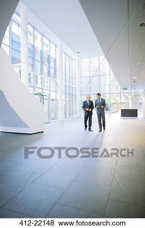 Stock Photo - Businessmen walking together in office building. Fotosearch
