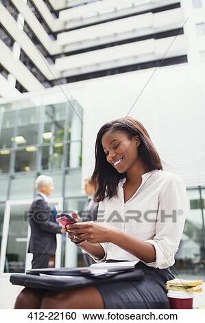 Businesswoman sitting on bench using cell phone outside View Large Photo Image Stock Image - Businesswoman sitting on bench using cell phone outside. Fotosearch