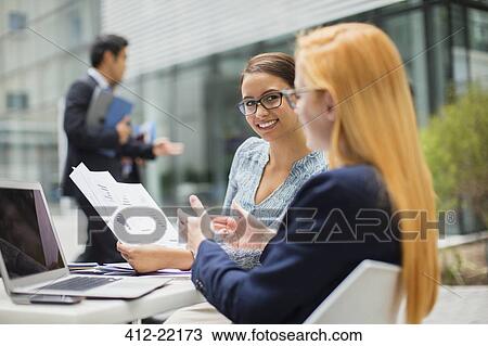 Stock Image - Businesswomen looking at documents at table in office building. Fotosearch