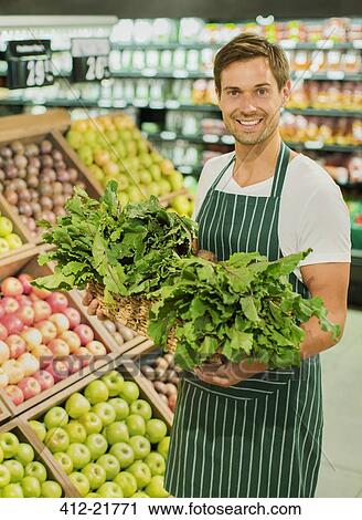 Stock Image - Clerk carrying basket of produce in grocery store. Fotosearch