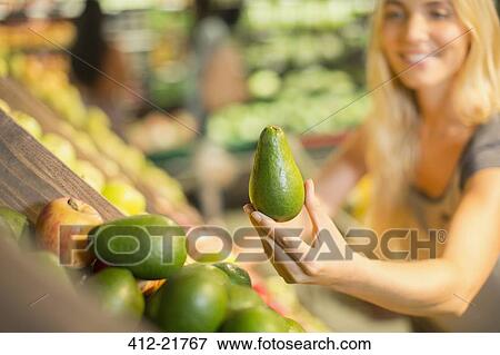 Stock Photo - Close up of woman holding produce in grocery store. Fotosearch