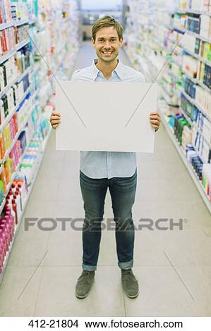 Picture - Man holding blank card in grocery store aisle. Fotosearch