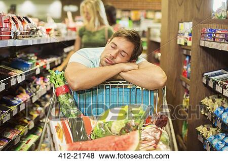 Stock Photo - Man sleeping on shopping cart in grocery store. Fotosearch