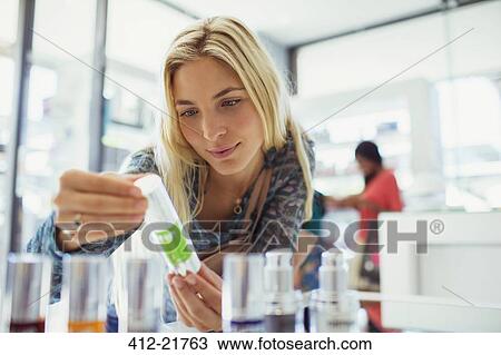 Stock Image - Woman examining skincare product in drugstore. Fotosearch