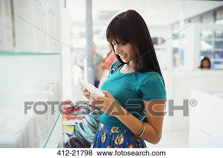 Woman examining skincare product in drugstore View Large Photo Image Stock Photo - Woman examining skincare product in drugstore. Fotosearch