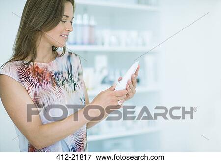 Woman examining skincare product in drugstore View Large Photo Image Stock Photo - Woman examining skincare product in drugstore. Fotosearch