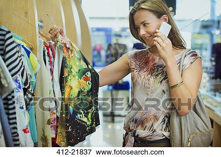 Woman talking on cell phone and shopping in clothing store View Large Photo Image Stock Photo - Woman talking on cell phone and shopping in clothing store. Fotosearch
