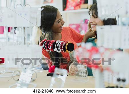Stock Image - Women trying on jewelry together in clothing store. Fotosearch