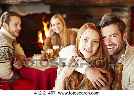 Stock Photo - Couple hugging at restaurant with friends. Fotosearch