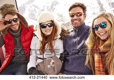 Stock Image - Friends smiling together on ski lift. Fotosearch