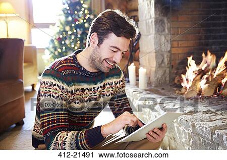 Stock Image - Man using digital tablet in front of fireplace. Fotosearch
