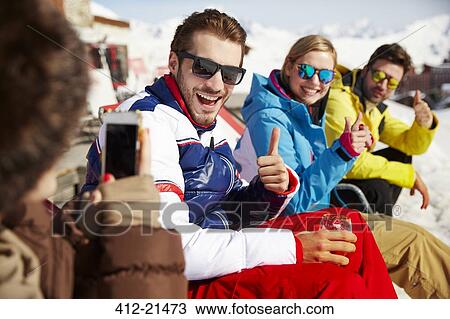Stock Image - Woman taking pictures of friends in the snow. Fotosearch