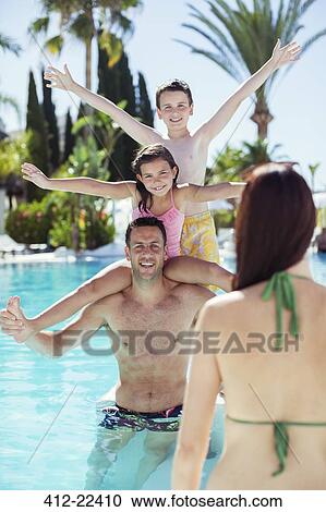 Stock Image - Father giving piggyback ride to his two children in swimming pool. Fotosearch