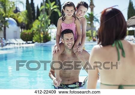 Stock Photo - Father giving piggyback ride to his two children in swimming pool. Fotosearch