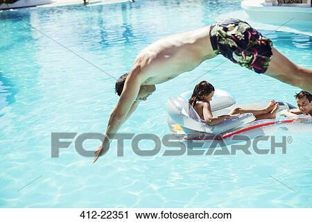 Stock Image - Man diving into swimming pool, children floating on air mattress in background. Fotosearch