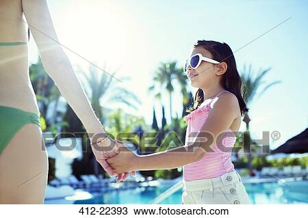 Stock Image - Mother and daughter holding hands by swimming pool. Fotosearch
