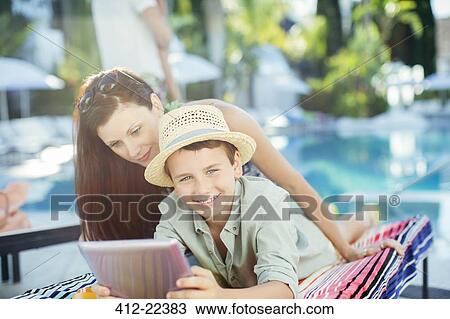 Stock Image - Mother and son using tablet pc by swimming pool. Fotosearch