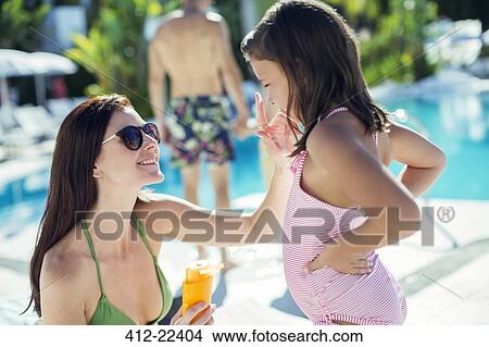 Picture - Mother applying suntan lotion on daughter's face by swimming pool. Fotosearch