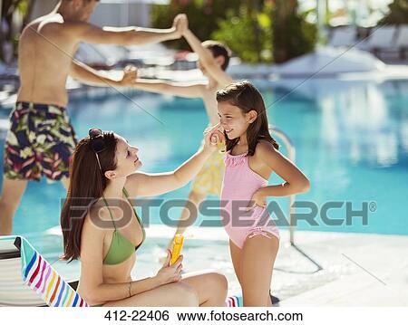 Stock Photograph - Mother applying suntan lotion on daughter's face by swimming pool. Fotosearch