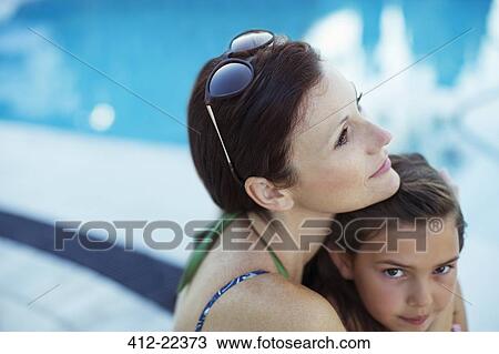 Stock Image - Pensive woman sitting by swimming pool with daughter. Fotosearch