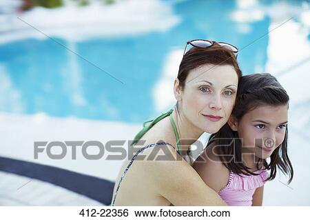 Stock Photograph - Portrait of mother and daughter sitting by swimming pool. Fotosearch