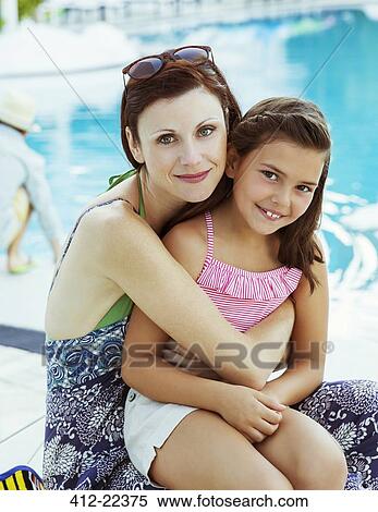 Stock Photography - Portrait of mother and daughter sitting by swimming pool. Fotosearch