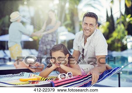 Stock Photo - Portrait of smiling father and daughter relaxing by swimming pool, mother and daughter in background. Fotosearch