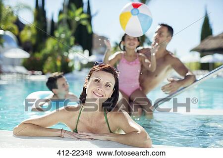 Portrait of smiling woman in swimming pool, family playing with beach ball in background View Large Photo Image Stock Photo - Portrait of smiling woman in swimming pool, family playing with beach ball in background. Fotosearch