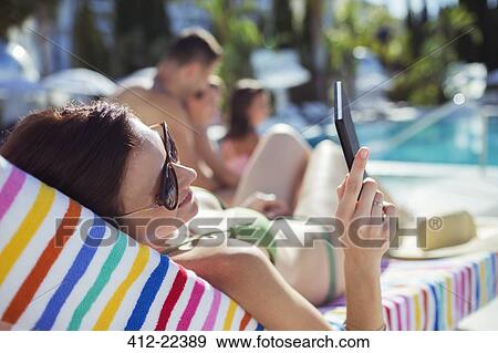 Stock Photo - Woman sunbathing and texting by swimming pool. Fotosearch