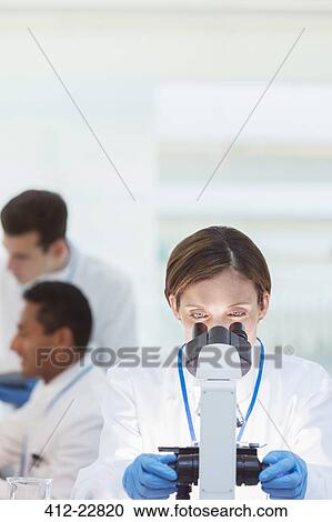 Stock Image - Scientist examining sample under microscope in laboratory. Fotosearch
