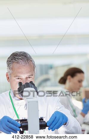 Stock Photo - Scientist examining sample under microscope in laboratory. Fotosearch