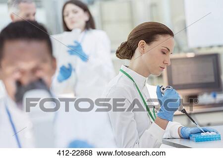 Scientist pipetting sample into tray in laboratory View Large Photo Image Stock Photo - Scientist pipetting sample into tray in laboratory. Fotosearch
