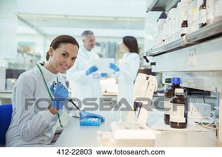 Stock Image - Scientist pipetting samples into tray in laboratory. Fotosearch