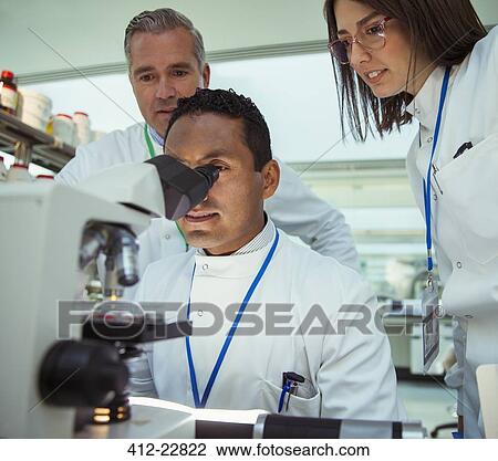 Stock Image - Scientists examining sample under microscope in laboratory. Fotosearch