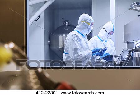Stock Image - Scientists in clean suits using digital tablets in experiment in laboratory. Fotosearch