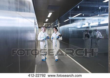 Stock Image - Scientists in clean suits walking in hallway. Fotosearch
