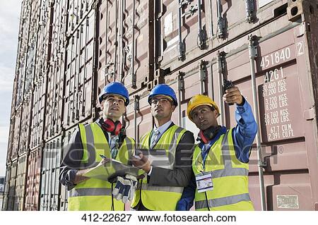 Stock Photo - Businessmen and worker talking near cargo containers. Fotosearch