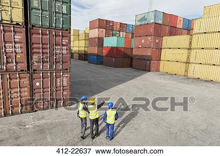 Stock Photo - Businessmen and worker talking near cargo containers. Fotosearch