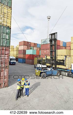 Stock Photo - Businessmen and worker talking near cargo containers. Fotosearch