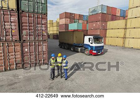 Stock Photo - Businessmen and worker talking near cargo containers. Fotosearch