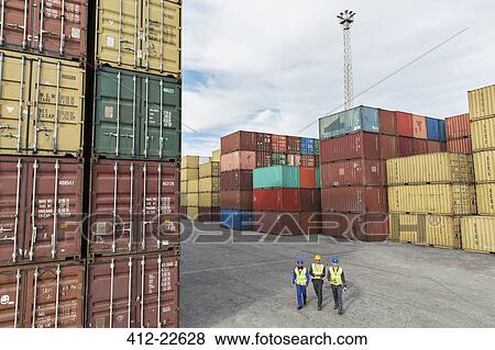 Stock Photo - Businessmen and worker walking near cargo containers. Fotosearch