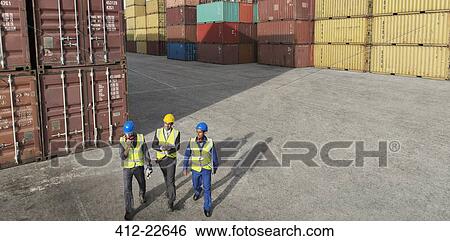 Stock Photograph - Businessmen and worker walking near cargo containers. Fotosearch