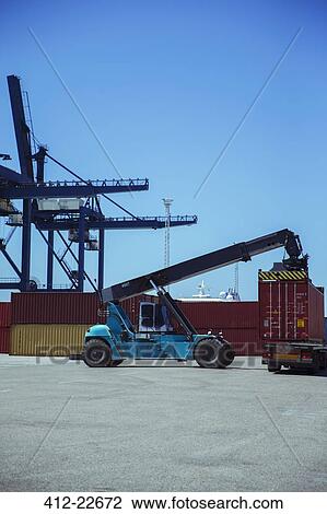Stock Image - Crane lifting cargo container onto truck. Fotosearch